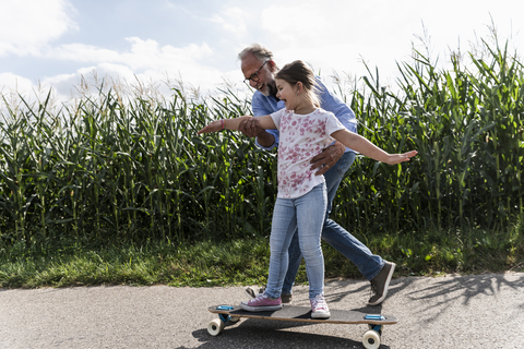 Älterer Mann hilft kleinem Mädchen, Skateboardfahren zu lernen, lizenzfreies Stockfoto