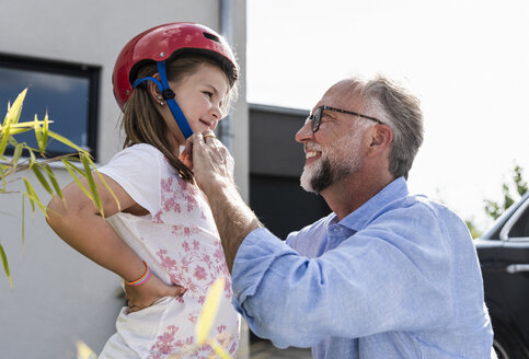 Mature man fixing safety helmet on little girl's head - UUF14563