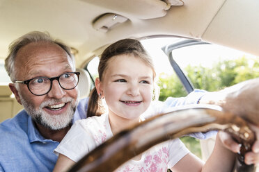 Little girl sitting on lap of grandfather, pretending to steer the car - UUF14565