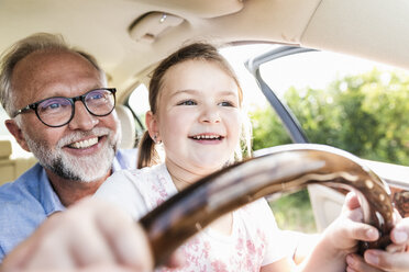 Little girl sitting on lap of grandfather, pretending to steer the car - UUF14566