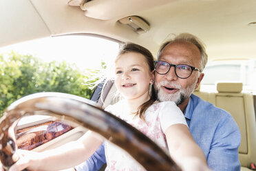 Little girl sitting on lap of grandfather, pretending to steer the car - UUF14567