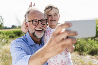 Mature man and little girl making fun selfies in the field - UUF14573