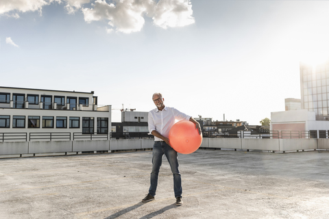 Mature man playing with orange fitness ball on rooftop of a high-rise building stock photo