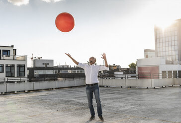 Älterer Mann spielt mit orangefarbenem Fitnessball auf dem Dach eines Hochhauses - UUF14637