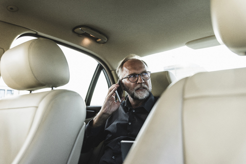 Älterer Geschäftsmann sitzt auf der Rückbank im Auto und telefoniert, lizenzfreies Stockfoto