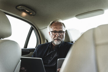 Älterer Geschäftsmann sitzt auf der Rückbank im Auto und benutzt ein digitales Tablet - UUF14641