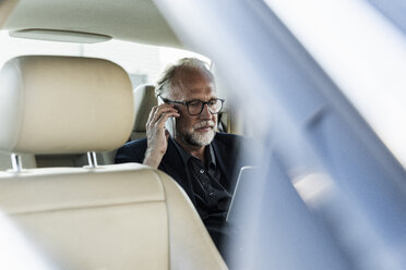 Älterer Geschäftsmann sitzt auf der Rückbank im Auto und telefoniert - UUF14643