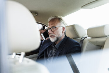 Älterer Geschäftsmann sitzt auf der Rückbank im Auto und telefoniert - UUF14649