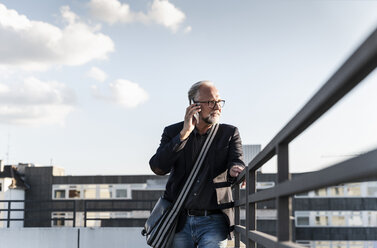 Älterer Mann steht auf einem Dach, stützt sich auf ein Geländer und benutzt ein Smartphone - UUF14653