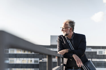 Mature man standing on rooftop, leaning on railing - UUF14654