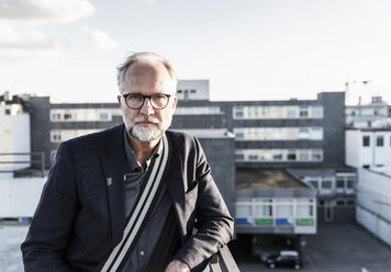 Mature man standing on rooftop, leaning on railing - UUF14656