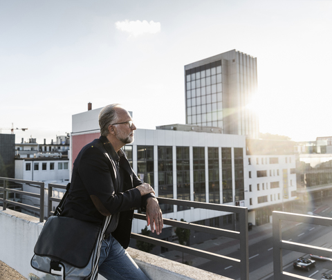 Älterer Mann steht auf einem Dach und stützt sich auf ein Geländer, lizenzfreies Stockfoto