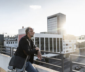 Mature man standing on rooftop, leaning on railing - UUF14658