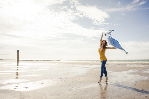 Glückliche Frau, die am Strand Spaß hat, tanzt und das Handtuch schwingt, lizenzfreies Stockfoto