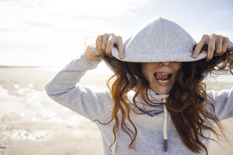 Frau, die sich an einem windigen Strand vergnügt, mit Kapuze, lizenzfreies Stockfoto