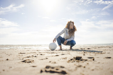 Frau mit Fußball am Strand hockend, wegschauend - KNSF04239