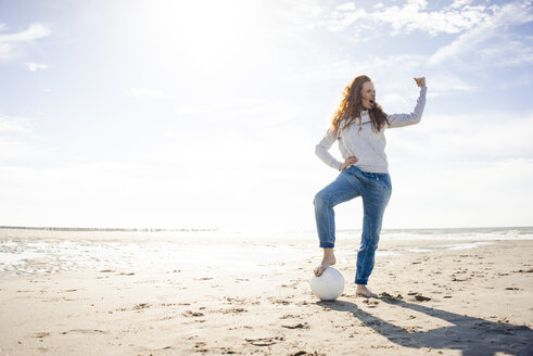 Happy woman having fun at the beach, flexing muscles, playing with soccer ball - KNSF04240