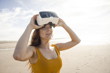 Redheaded woman using VR glasses on the beach - KNSF04253