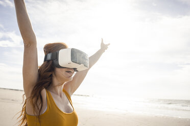 Redheaded woman using VR glasses on the beach - KNSF04254