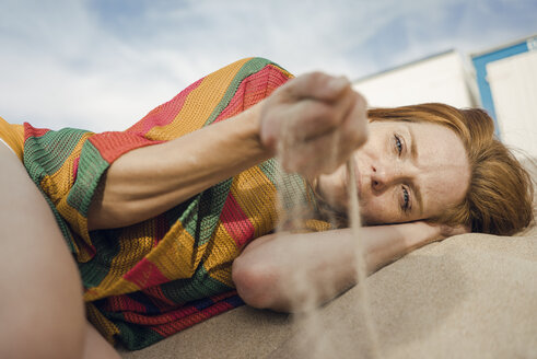 Redheaded woman lying on the beach, with sand trickling through her hand - KNSF04258