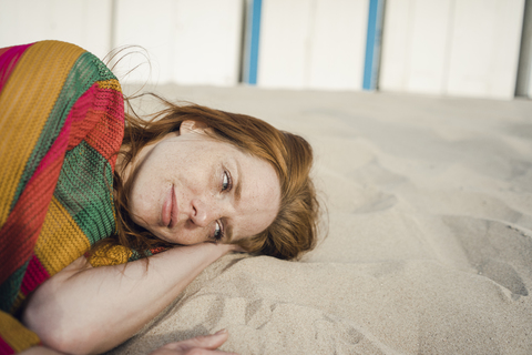 Rothaarige Frau ruht sich im Sand am Strand aus, lizenzfreies Stockfoto