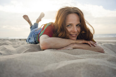 Rothaarige Frau liegt lächelnd im Sand am Strand - KNSF04265