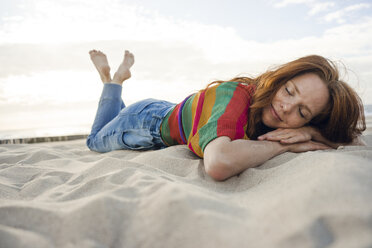 Redheaded woman lying in sand on the beach, with eyes closed - KNSF04266