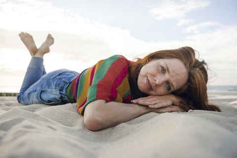 Redheaded woman lying in sand on the beach stock photo