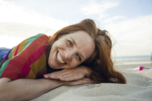 Redheaded woman lying in sand on the beach, with eyes closed - KNSF04268