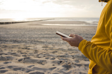 Man in yellow jacket, using smartphone on the beach - KNSF04270