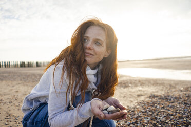Redheaded woman collecting shell on the beach - KNSF04272