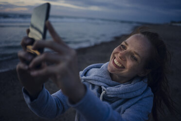 Woman using smartphone on the beach at sunset - KNSF04277