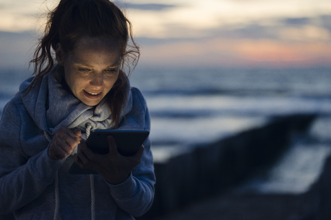 Frau mit digitalem Tablet am Strand bei Sonnenuntergang, lizenzfreies Stockfoto