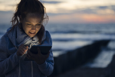 Woman using digital tablet on the beach at sunset - KNSF04280