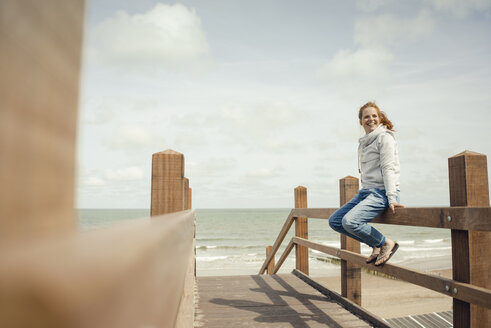 Frau sitzt am Zaun am Meer und lächelt - KNSF04295