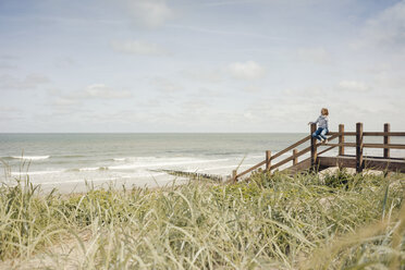 Frau sitzt auf einem Zaun am Strand und entspannt sich am Meer - KNSF04296