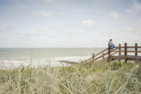 Woman sitting on fence at the beach, relaxing at the sea - KNSF04297