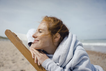 Lächelnde Frau im Liegestuhl liegend, die ein Sonnenbad am Strand genießt - KNSF04301