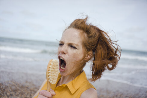 Woman using hair brush at the sea as a microphone - KNSF04304