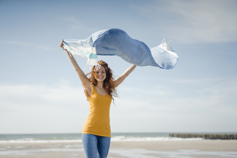 Glückliche Frau, die am Strand Spaß hat, tanzt und das Handtuch schwingt, lizenzfreies Stockfoto