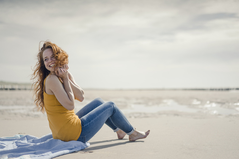 Frau sitzt am Strand und lacht, lizenzfreies Stockfoto