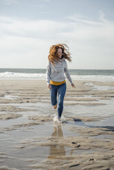 Glückliche Frau, die sich am Strand amüsiert, läuft am Meer - KNSF04319