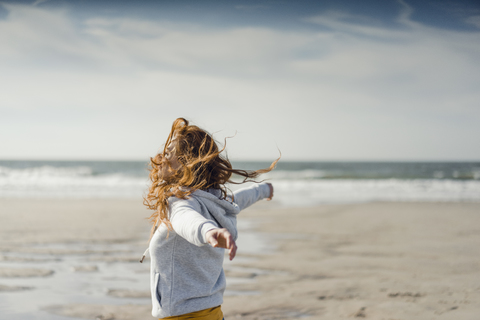 Rothaarige Frau entspannt sich am Strand, mit ausgestreckten Armen, lizenzfreies Stockfoto