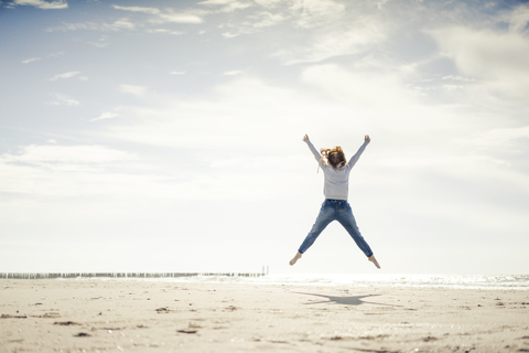 Happy woman having fun at the beach, jumping in the air stock photo