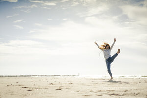 Glückliche Frau, die am Strand Spaß hat und im Sand tanzt - KNSF04326