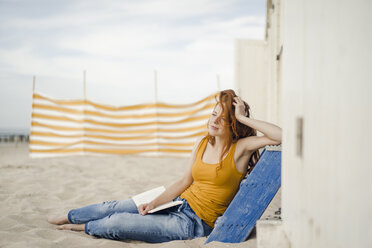 Rothaarige Frau sitzt vor einer Strandhütte und liest ein Buch - KNSF04331