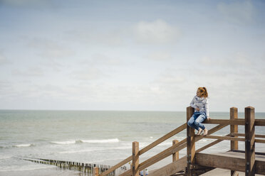 Woman sitting on fence at the beach, relaxing at the sea - KNSF04337