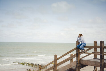 Frau sitzt auf einem Zaun am Strand und entspannt sich am Meer - KNSF04338