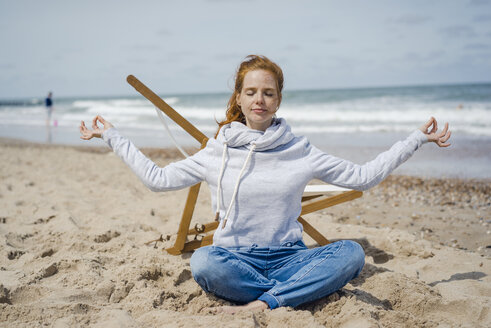 Woman sitting cross-legged on sand, meditating on the beach - KNSF04341