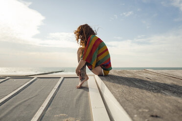 Frau mit Tätowierung hockt auf einer Planke und blickt auf das Meer - KNSF04343